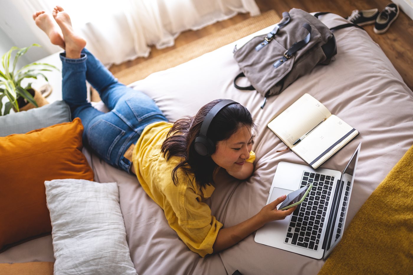 College student chills on her bed while on her laptop and wearing headphones