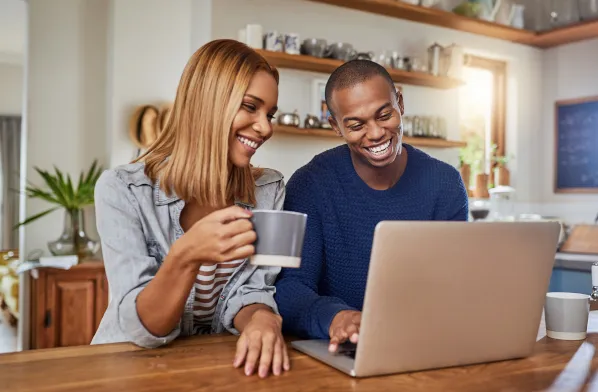 An older man smiles up from his desk while typing on his laptop