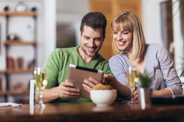A young couple drink champagne while smiling at an iPad